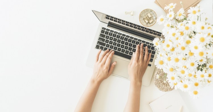 Photo of someone typing at a laptop with a big bunch of daisies
